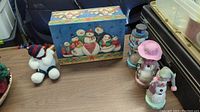 Photo showing all items on table: decorative holiday box with snowmen illustration and four snowman figurines with various hats and scarves