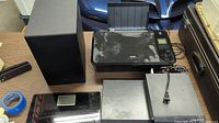 Lot items including black Samsung subwoofer, Canon Pixma printer, multiple DVD players, and digital scale arranged on a table with visible power cords and accessories.