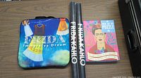 Frida Kahlo seat cushion, two rolled posters, and puzzle box on a wood surface.