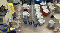 Top view showing six clear etched glass goblets, three blue tinted glasses, and multiple ceramic mugs in white, red, and maroon