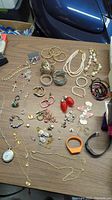 Top view showing a variety of costume jewelry items on a table: bangles, bracelets, necklaces including pearls, rings, earrings, and wristwatches. Jewelry boxes empty.