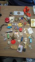 Top view of a large variety of keychains and keys spread on a wooden surface showing multiple items including novelty, branded, decorative, and metal keys.