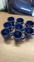 Seven blue Corelle stoneware mugs arranged in a group on a wooden surface