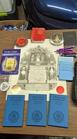Photo of Masonic books, pins, buttons, and pamphlets arranged on a table.