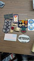 Photo of various military patches, medals, stickers, and decals arranged on a wooden surface.