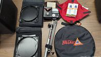 Various photo equipment and accessories including bellows, filters, light meter, film canisters, tripod, and diffuser case.