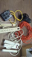 Lot of various power strips and extension cords on wooden surface, showing cords and outlet switches