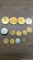 Top view of the lot of 13 metal tokens and coins of different sizes, materials, and designs arranged on a wooden surface.