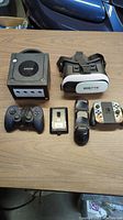 Lot items arranged on table: Nintendo GameCube console, two controllers (GameCube wired and Nintendo Switch grip), Rokz VR headset, and Xbox 360 S Hard Drive.