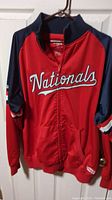 Front view of red and navy Washington Nationals jacket with 'Nationals' script across the chest, full zipper, and ribbed collar/cuffs.