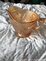Single photo showing the antique carnival glass creamer in golden iridescent finish with iris floral pattern and ribbed texture.