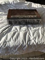 Photo of a brown vintage clock radio placed on a white quilted fabric showing front digital display and buttons on top with sunlight casting shadows.