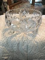 Photo of a large crystal bowl showing intricate cut leaf and diamond patterns, scalloped rim, and three paw-shaped feet.