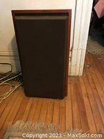 Front view of one speaker showing wooden cabinet and fabric grille