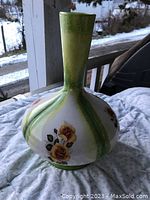 Photo of a ceramic vase with a bulbous base and tall slender neck. Vase shows hand-painted yellow roses with green leaves on a white background, with green shading at top and base.
