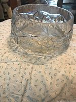 Clear vintage crystal bowl showing detailed cut starburst and geometric patterns on its side, placed on fabric background.