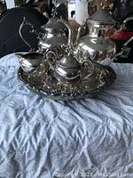 Photo showing vintage silver plated tea service with five pieces including teapot, coffee pot, creamer, sugar bowl, all on an ornate serving tray.
