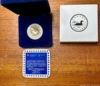 1987 Canadian Loonie coin in glass capsule inside blue velvet presentation case, with cardboard box and informational card visible