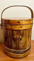 Front view of round antique wooden sugar bucket with handle, lid, and faded advertising on side
