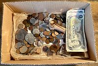 Box with a large number of mixed circulated coins in various sizes and a bundle of Canadian one-dollar banknotes.