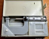 Precision micrometer MK 25-50mm housed in a gray plastic storage case. Micrometer spindle and thimble visible, thimble labelled USSR 0.01mm, the micrometer is placed snugly inside the molded case insert.