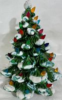 Front view of the ceramic Christmas tree showing green branches, white snow accents, and colored light bulbs.