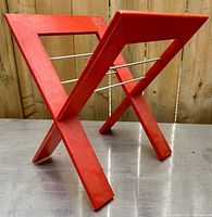 Side angle showing the X-shaped wooden frame with red stain and silver metal rods between the frames.