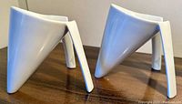 Side view of the two white porcelain mugs showing the angled double handle/stands design and triangular body shape.