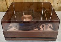 Front view of turntable inside tinted dust cover, showing Noresco logo on wood veneer cabinet