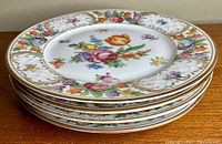 Stack of six porcelain plates with multicolor floral designs and gold decoration on rims.