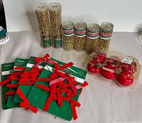 Photo showing several clear plastic tubes with gold bead garlands plus four packs of red ribbon bows and a package of red bell ornaments.