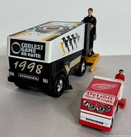 Front and side view of two vintage Zamboni toy models with drivers and NHL logos visible.