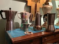 Four stovetop espresso machines and extra rubber rings on table, showcasing metal and ceramic materials, varying sizes and shapes