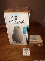 Photo of the boxed gray Homedics Ellia aroma diffuser next to a small box containing 3-pack essential oils on wooden surface