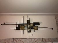 Straight on view of the metal wall art, showing the overall composition of the rectangular and square metal plates mounted on thin rods.