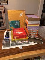 Entire lot arranged on table showing stacked colored paper, envelopes, stapler, hole punch, and metal containers with staples and paper clips.