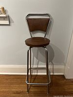 Front view of the mid-century modern swivel stool showing round brown vinyl seat and backrest with chrome frame.
