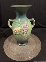 Front view of Roseville Pottery vase showing green glaze and purple and cream freesia flowers in relief with dual handles.