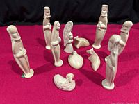 Front view of all 11 carved stone nativity figures arranged on red cloth background including human figures, baby Jesus, and animals.