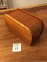 Side angled view of teak tambour roll top box showing wood grain and tambour slats closed, placed on wooden surface.