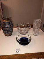 Four items displayed on table: ceramic vase with blue teardrop pattern, two glass bowls, and one tall textured glass vase.