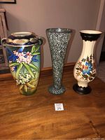 Three vases displayed side by side on a wood surface, showing full shapes and decorations