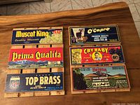Top-down photo of six wine grape crate panels with colorful vintage labels arranged on a wooden floor.