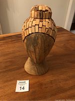 Angled side view of the wooden head sculpture showing the texture and details of the block hair design and smooth faceless wooden face.