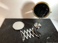 Tabletop mirror standing on base and wall-mounted mirror fully collapsed on table showing both mirrors.