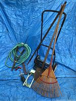 Photo of assorted gardening tools including rake, hose with nozzle, hand pruner, and reel mower handle and wheels visible