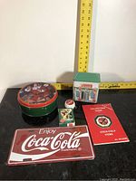 All Coca-Cola memorabilia items displayed on black surface with measuring tape for scale.