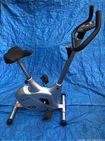 Right side view of the compact silver exercise bike showing seat, pedals, handlebars, and frame.