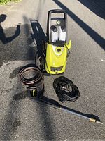 Full view of the yellow and black electric power washer with spray gun, multiple cables, and hose.