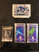 Stack of Upper Deck hockey cards, and two unopened Skybox NBA basketball card packs with blue and green star and lightning bolt designs, placed on black surface.